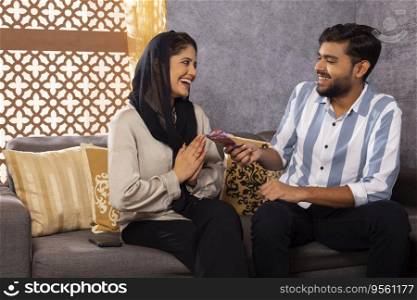 Husband giving money to his wife while sitting on sofa at home