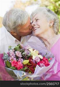 Husband giving wife flowers outdoors kissing and smiling