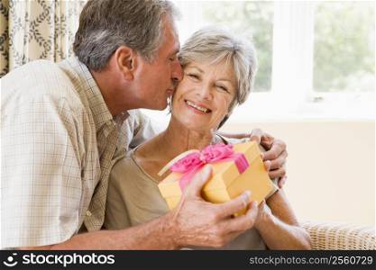 Husband giving wife gift in living room kissing her and smiling