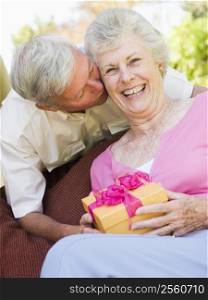 Husband giving wife gift on patio kissing her and smiling