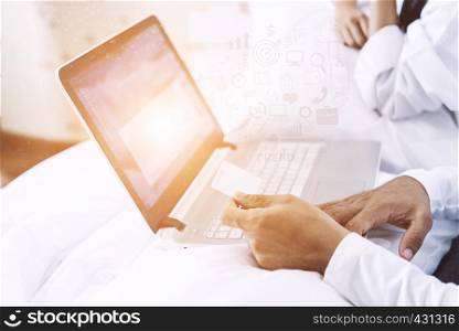 Husband hand holding a credit card and using a laptop for working or online purchasing on bedroom in the morning at home. Online business concept.