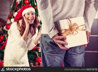Husband hiding behind a gift from his wife, with pleasure receiving Christmas present, happy family holidays at home