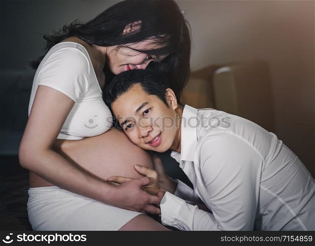 Husband listening to his wife&rsquo;s belly on a bed