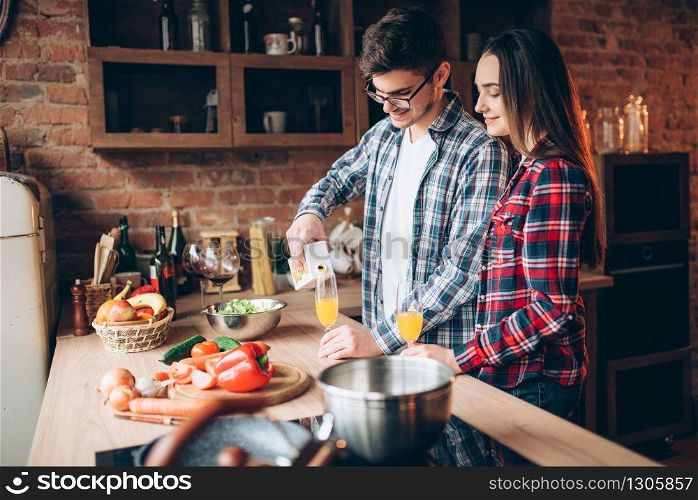 Husband pours fresh fruit juice in a glass, family cooking romantic dinner together. Couple prepares healthy food dinner together. Vegetable salad preparation on the kitchen