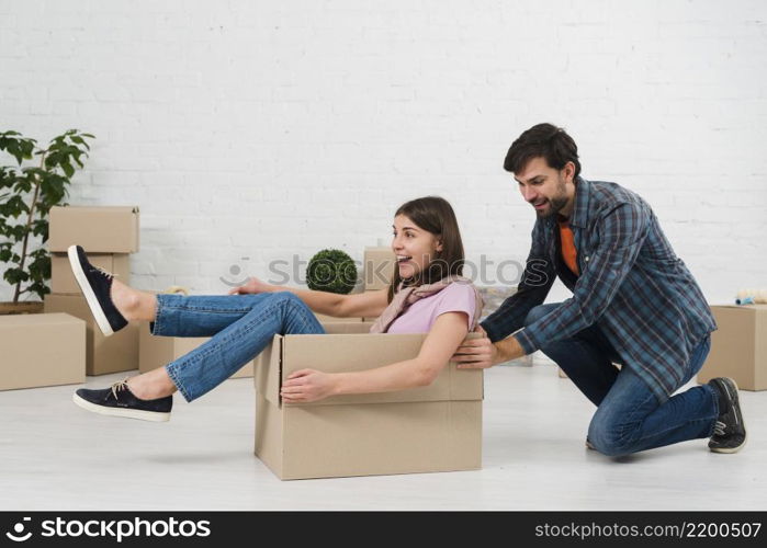 husband pushing his wife sitting cardboard box