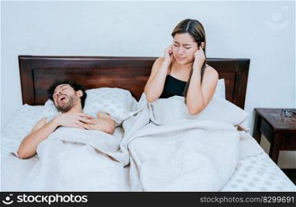Husband snoring while the wife suffers and covers her ears. Sleep apnea concept, Snoring man in bedroom and wife covering her ears