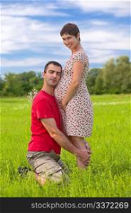 Husband taking care of his pregnant wife on the green meadows