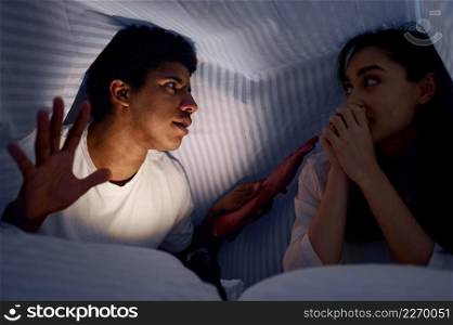 Husband telling wife mysterious scary story lying under blanket. Family having fun before night. Husband telling wife scary story for under blanket