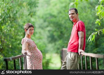 Husband with his pregnant wife on the bridge in green forest