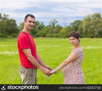 Husband with his pregnant wife on the green meadows
