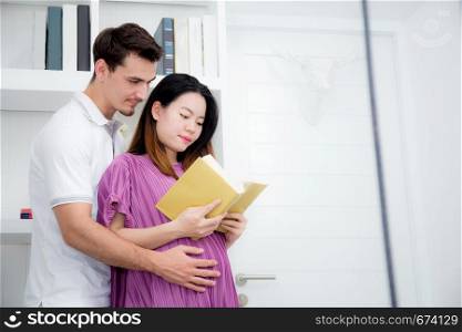 Husband with pregnant woman reading yellow book together, Portrait of couple with hug, happy with family choose name newborn concept.