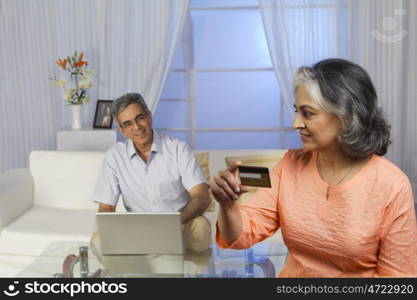 Husband working on the laptop while wife holds the credit card