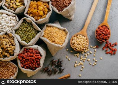 Husbandry and nutrtion concept. Top view of various beans and colorful dried fruit packed in little burlap sacks. Wooden spoon with ingredients