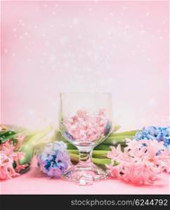 Hyacinths flowers and glass hearts in wineglass over light pink background. Spring greeting card.