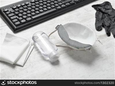hydro alcoholic gel , dust mask gloves and handkerchiefs on a desk with keyboard . hydroalcohol gel , dust mask gloves and handkerchiefs on a desk with keyboard