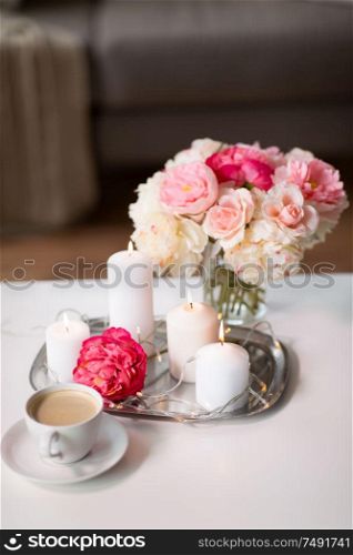 hygge and aromatherapy concept - burning candles, electric garland lights, cup of coffee and flowers on table. coffee, candles, garland and flowers on table
