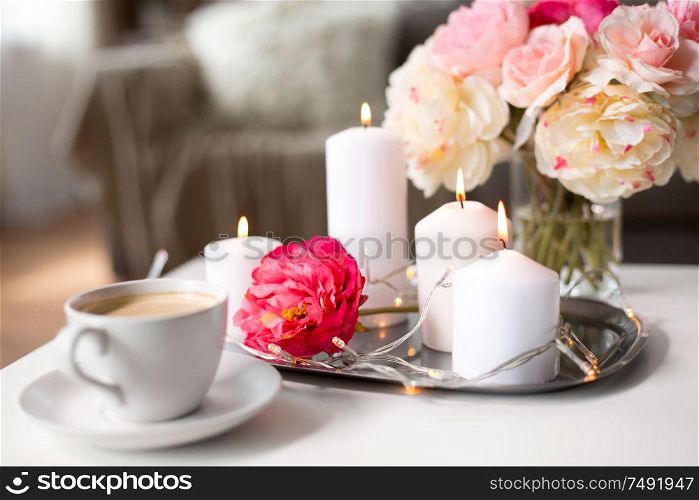 hygge and aromatherapy concept - burning candles, electric garland lights, cup of coffee and flowers on table. coffee, candles, garland and flowers on table