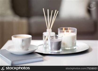 hygge and aromatherapy concept - coffee, candles and aroma reed diffuser on table at home. coffee, candles and aroma reed diffuser on table