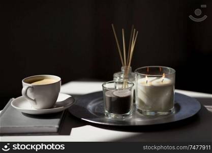 hygge and aromatherapy concept - coffee, candles, book and aroma reed diffuser on table. coffee, candles and aroma reed diffuser on table