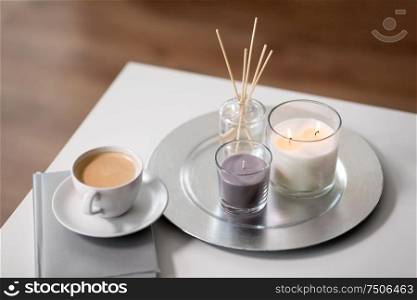 hygge and aromatherapy concept - coffee, candles, book and aroma reed diffuser on table. coffee, candles and aroma reed diffuser on table