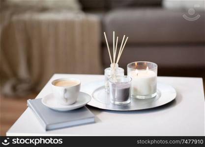 hygge and aromatherapy concept - coffee, candles, book and aroma reed diffuser on table at home. coffee, candles and aroma reed diffuser on table