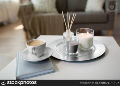 hygge and aromatherapy concept - coffee, candles, book and aroma reed diffuser on table at home. coffee, candles and aroma reed diffuser on table