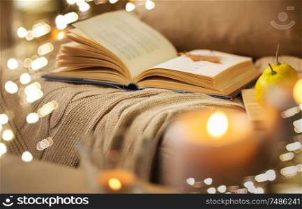 hygge and cozy home and literature concept - book with autumn leaf and blanket on sofa. book with autumn leaf and blanket on sofa at home