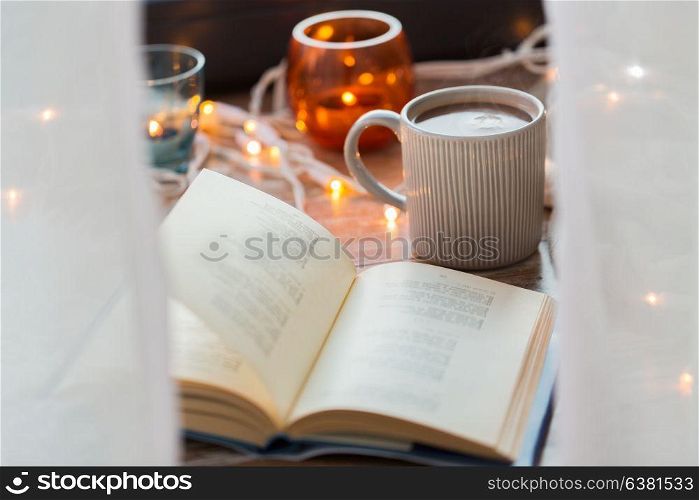 hygge and cozy home concept - book and cup of coffee or hot chocolate on table. book and cup of coffee or hot chocolate on table