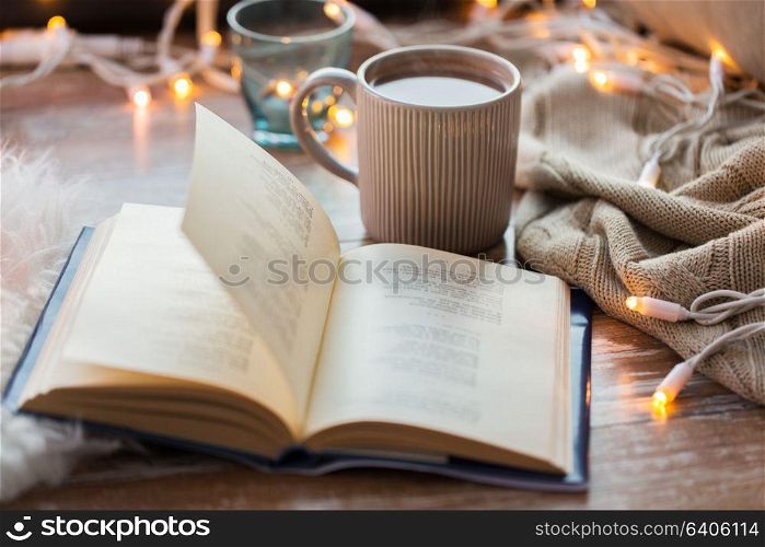 hygge and cozy home concept - book and cup of coffee or hot chocolate on table. book and cup of coffee or hot chocolate on table