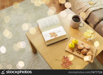 hygge and cozy home concept - book, autumn leaves, cup of tea with lemon, almond nuts and oatmeal cookies on table. book, lemon, tea and cookies on table at home