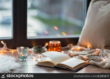 hygge and cozy home concept - book, garland lights and candles on window sill. book, garland lights and candles on window sill