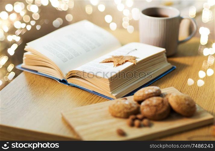 hygge and cozy home concept - book with autumn leaf, cup of tea and oatmeal cookies on wooden table. book with autumn leaf, cookies and tea on table