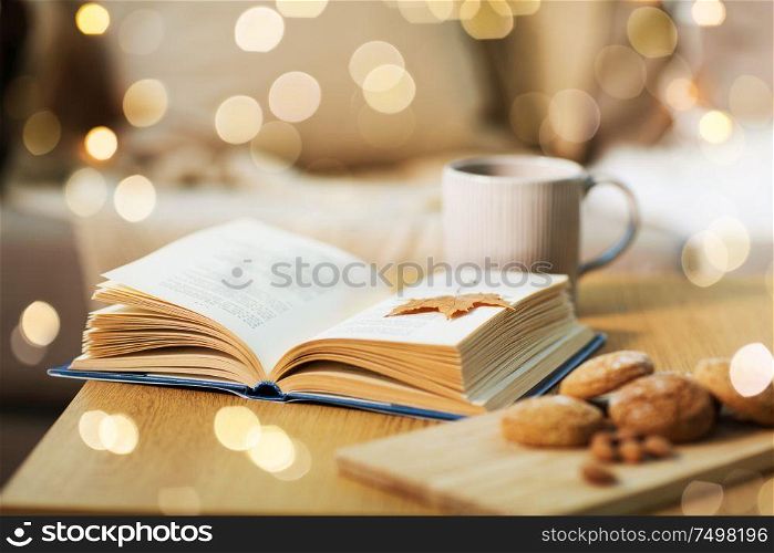 hygge and cozy home concept - book with autumn leaf, cup of tea and oatmeal cookies on wooden table. book with autumn leaf, cookies and tea on table