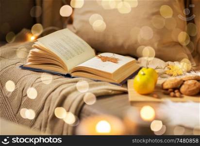 hygge and cozy home concept - book with autumn leaf, lemons and oatmeal cookies on sofa. book with autumn leaf and blanket on sofa