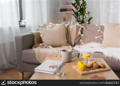 hygge and cozy home concept - cup of tea with lemon, book, autumn leaves and oatmeal cookies on wooden table in living room. tea with lemon, book and cookies on table at home