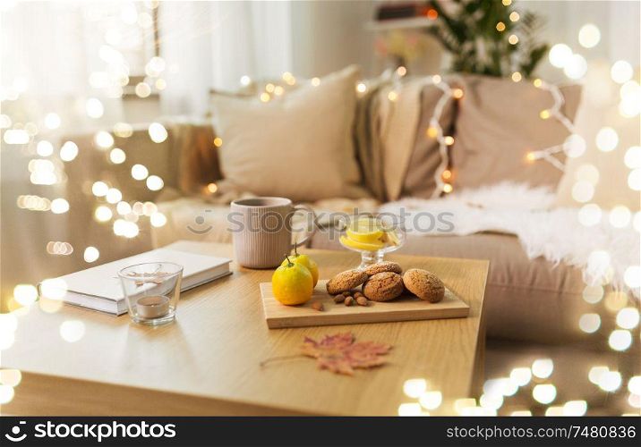 hygge and cozy home concept - oatmeal cookies, book, tea and lemon on wooden table in living room. oat cookies, book, tea and lemon on table at home