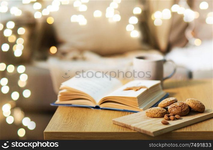 hygge, bake and food concept - oatmeal cookies, almonds, book and tea on wooden table at home. oat cookies, almonds and book on table at home