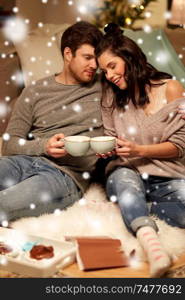 hygge, christmas and people concept - happy couple drinking hot chocolate with marshmallow and hugging at home over snow. happy couple drinking hot chocolate on christmas