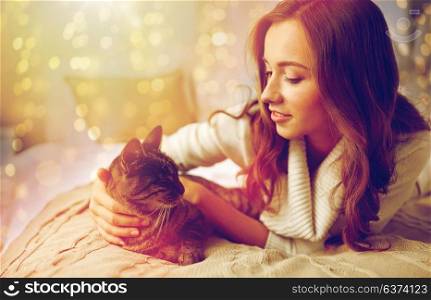 hygge, christmas, pets and people concept - happy young woman with cat lying in bed at home. happy young woman with cat lying in bed at home
