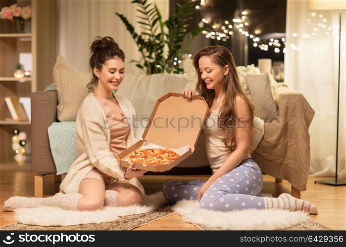 hygge, food and pajama party concept - happy female friends or teenage girls with pizza at home. happy female friends with pizza at home