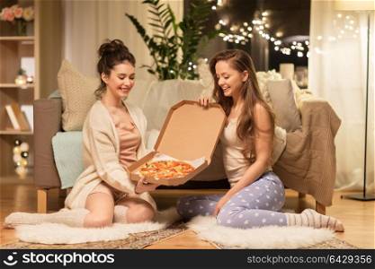 hygge, food and pajama party concept - happy female friends or teenage girls with pizza at home. happy female friends with pizza at home