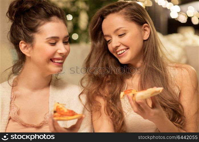 hygge, food and pajama party concept - happy female friends or teenage girls eating pizza at home. happy female friends eating pizza at home