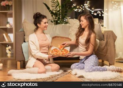 hygge, food and pajama party concept - happy female friends or teenage girls with pizza at home. happy female friends with pizza at home. happy female friends with pizza at home