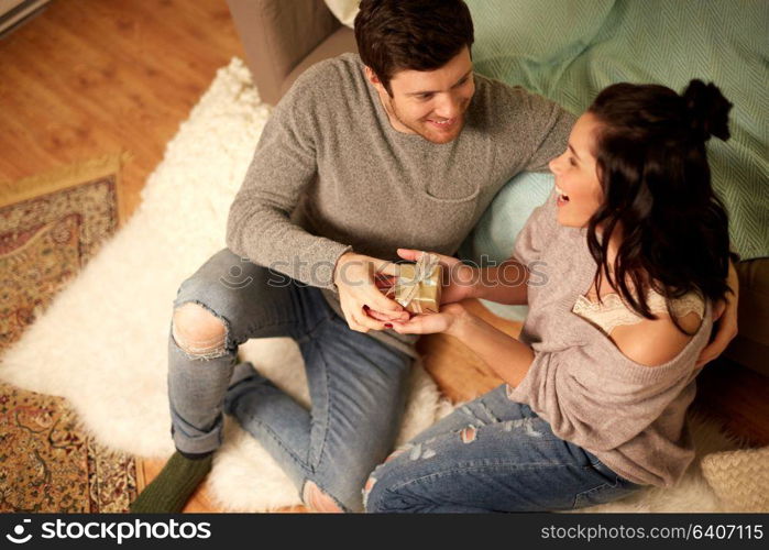 hygge, holidays and people concept - happy couple with gift box at home. happy couple with gift box at home