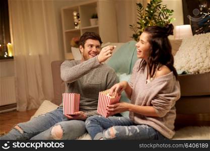 hygge, leisure and people concept - happy couple eating popcorn at home. happy couple eating popcorn at home