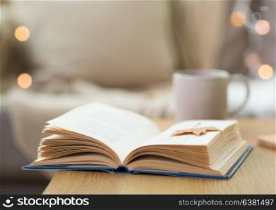 hygge, literature and reading concept - open book with autumn leaf on wooden table at home . book with autumn leaf on wooden table at home