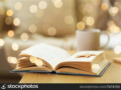hygge, literature and reading concept - open book with autumn leaf on wooden table at home. book with autumn leaf on wooden table at home