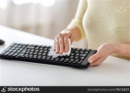 hygiene and disinfection concept - close up of woman cleaning computer keyboard with paper tissue. close up of woman cleaning keyboard with tissue
