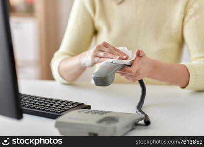 hygiene and disinfection concept - close up of woman hands cleaning desk phone with paper tissue. close up of woman cleaning desk phone with tissue