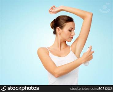 hygiene, bodycare and people concept - beautiful young woman applying antiperspirant or spray deodorant over blue background. woman with antiperspirant deodorant over blue